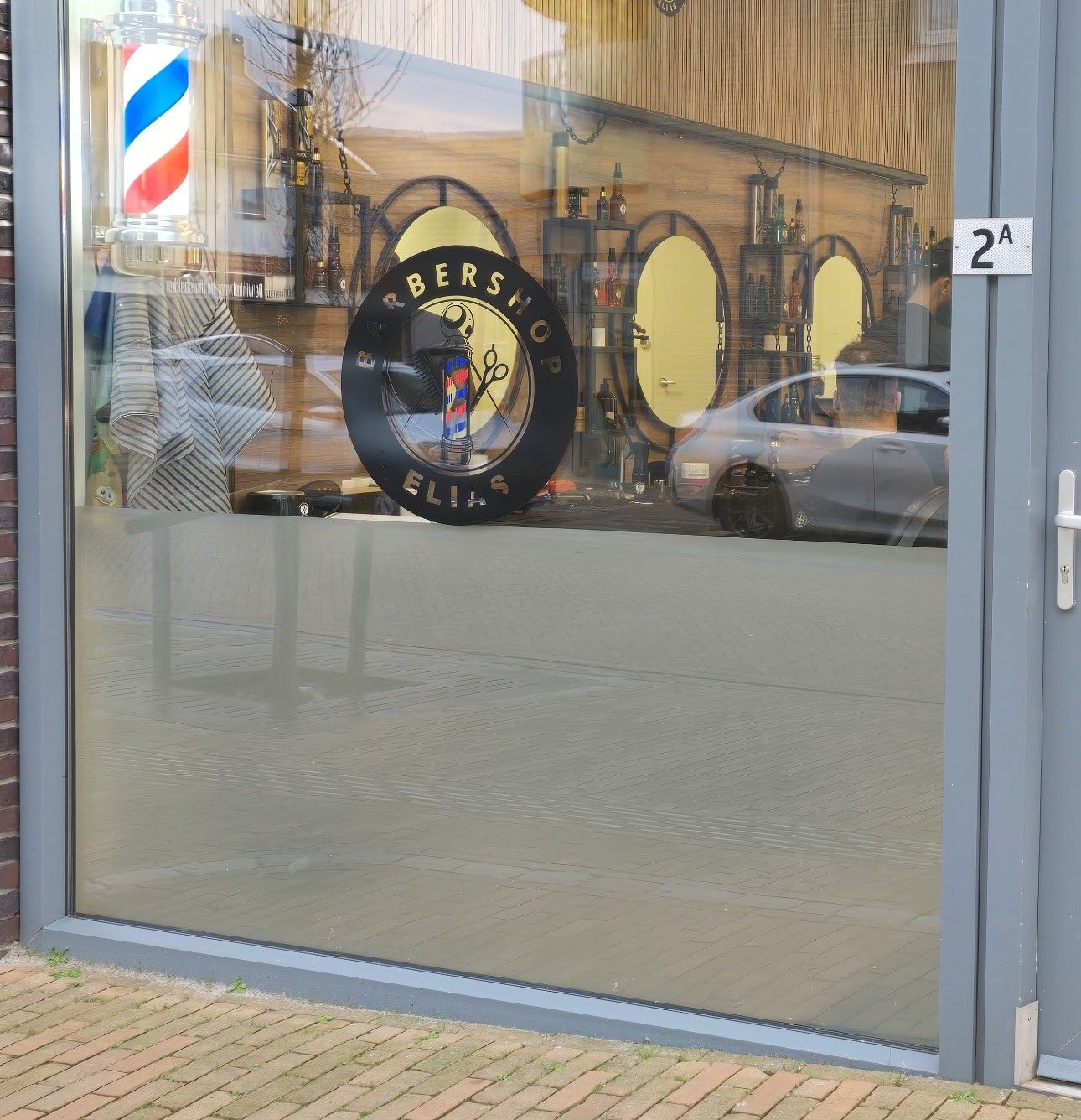 Glazen pui van Barbershop Elias met het ronde logo op het raam en huisnummer 2A